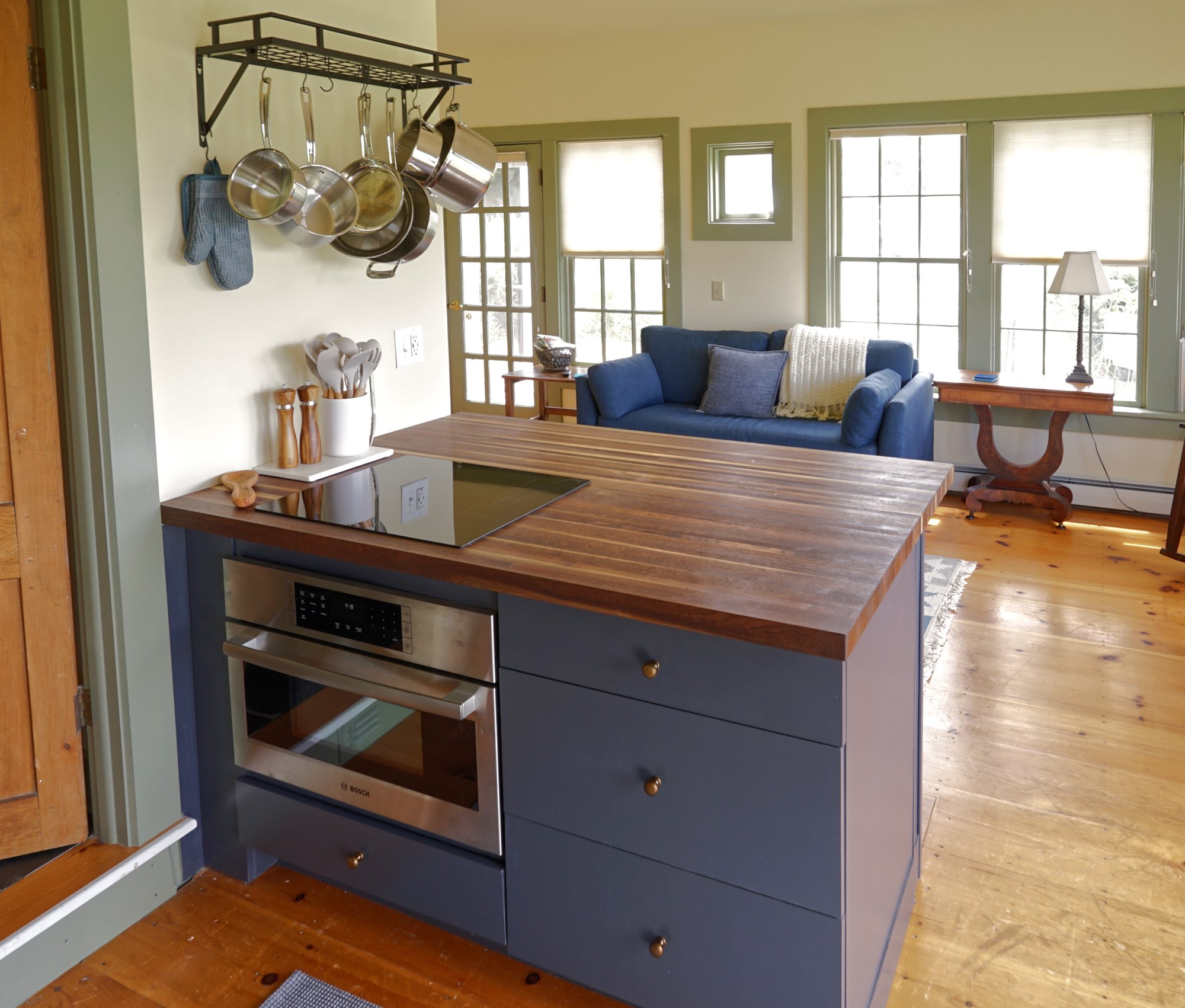 Butcher-block kitchen island with induction cooktop and built-in oven, with the blue sofa and living area beyond.
