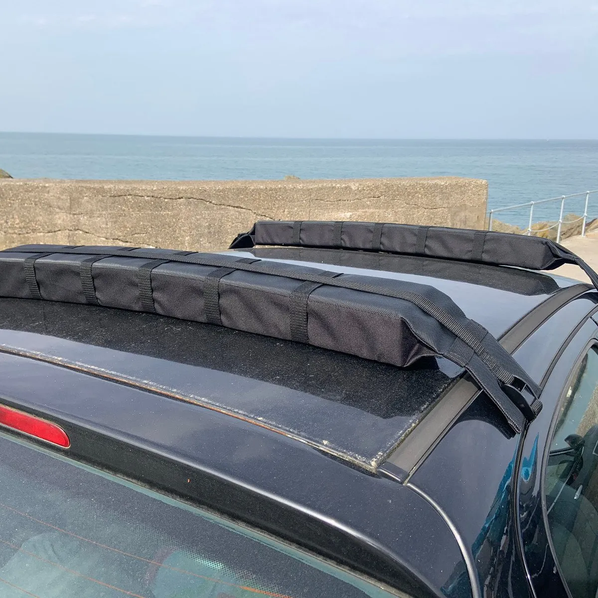 Two black foam soft roof-rack pads strapped across a car roof, ready for a kayak